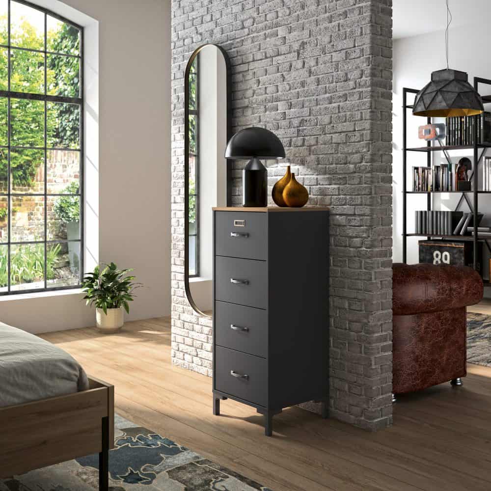 Manchester Smalle Ladekast - Zwart / Eiken Look met vier lades, passend voor industrieel interieur, zichtbaar naast een bed en potted plant in een stijlvolle kamer.