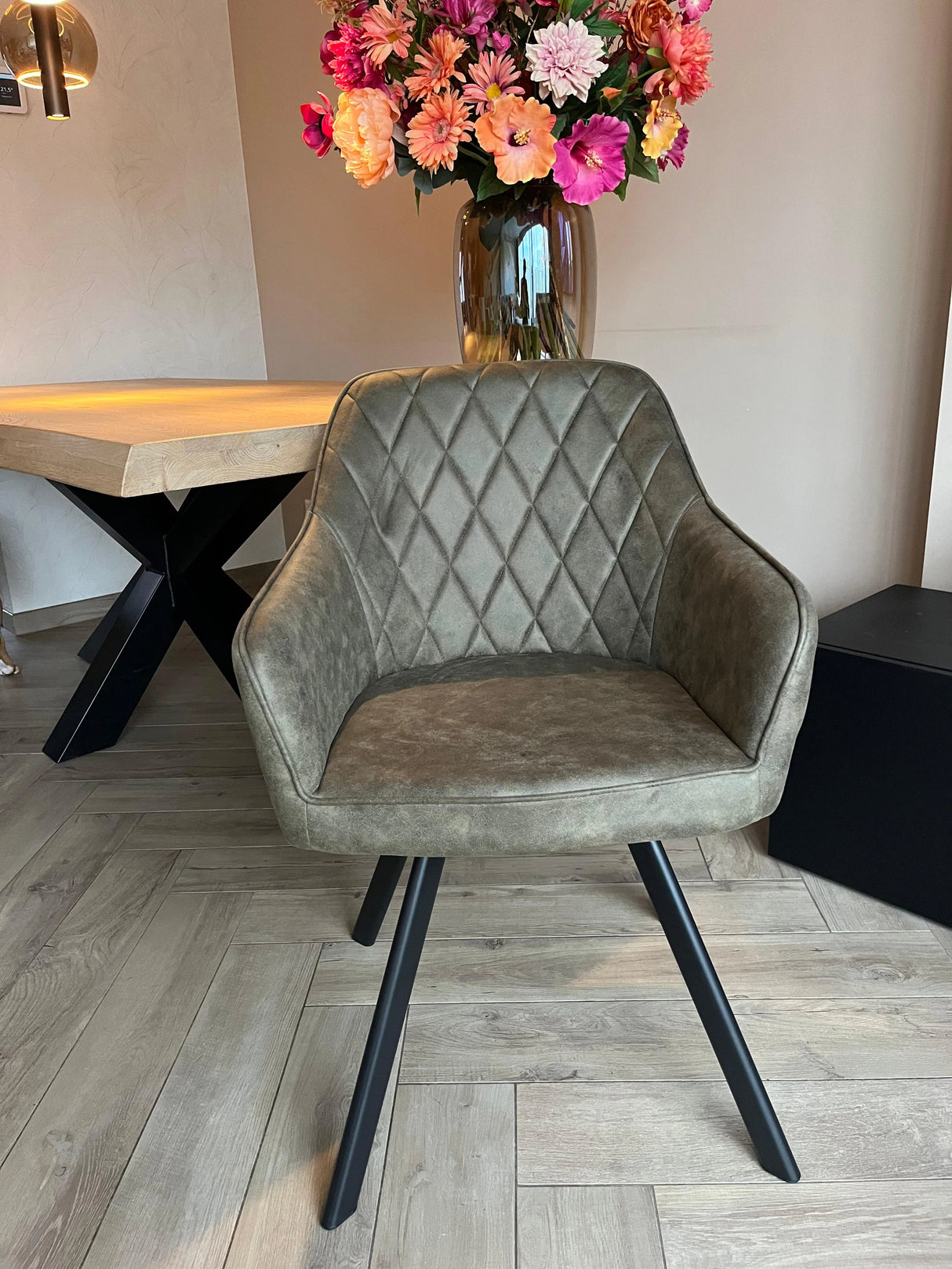 Eetkamerstoel Draaibaar 'Brione' met olijfgroene microvezel bekleding, diamantgestikte rugleuning en zwarte metalen poten, geplaatst op een lichte houten vloer.