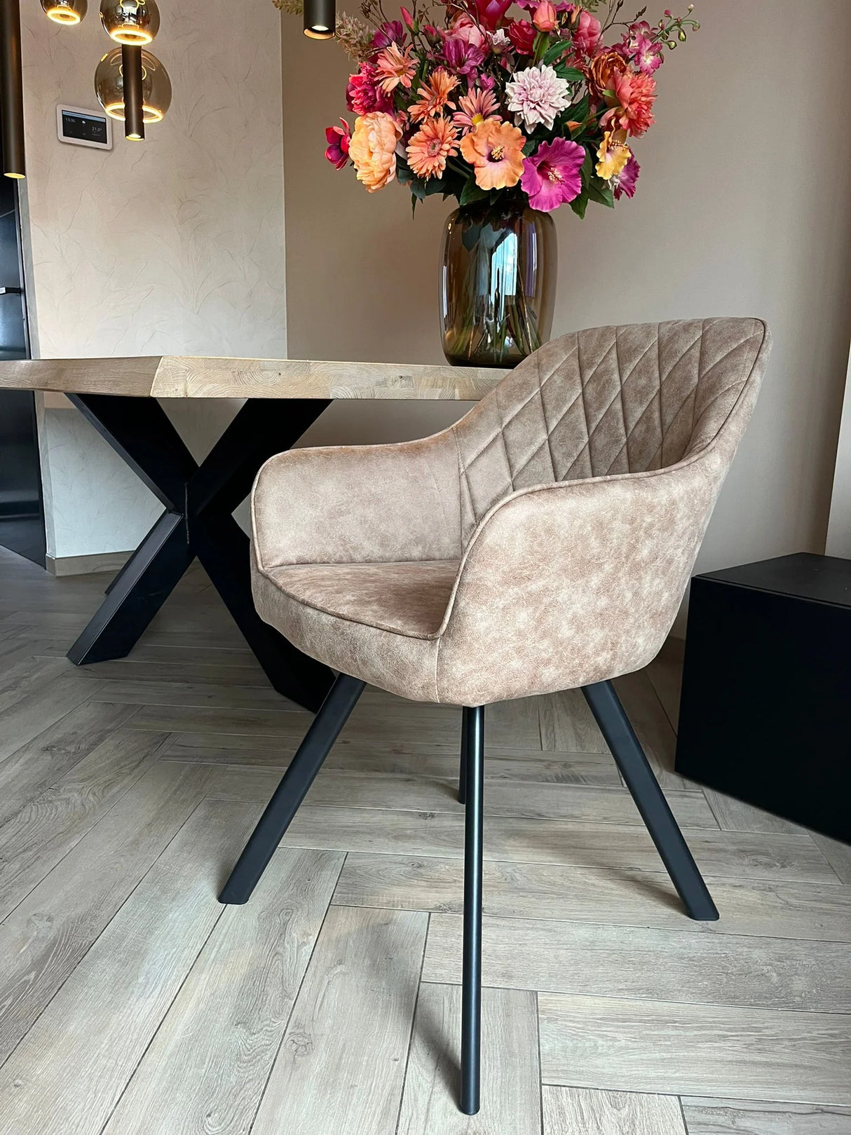 Eetkamerstoel Draaibaar 'Brione' met gestoffeerde rugleuning en slank zwart frame, geplaatst bij een houten tafel met kleurrijk bloemstuk.