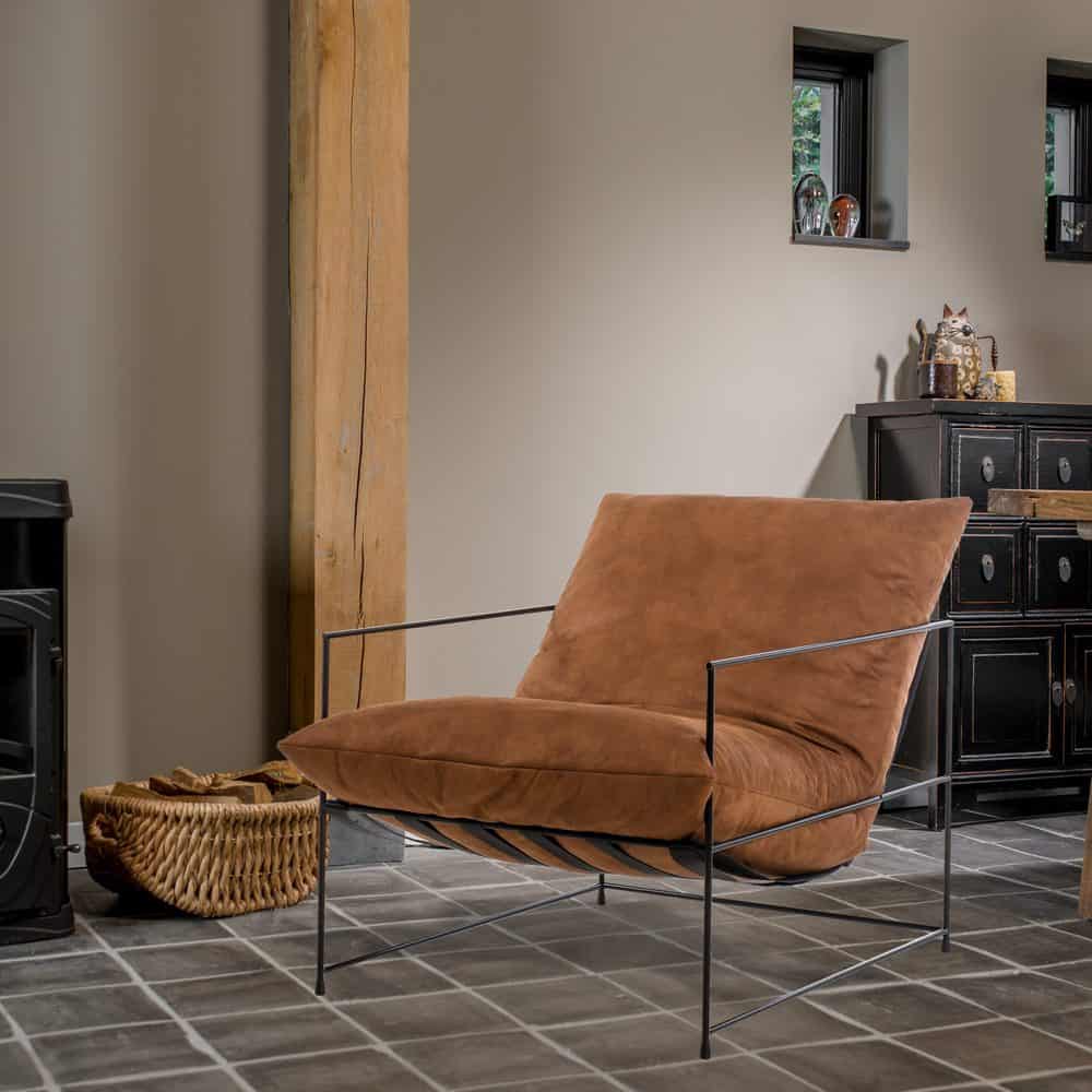 Fauteuil Elton - Bruin powdercoated PU leer in een moderne kamer, met zwart metalen frame en comfortabele zitting, perfect voor een loftinterieur.