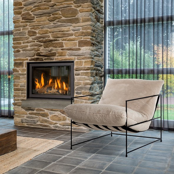 Fauteuil Elton - Wit Teddy Stof, een luxe stoel met zwart metalen frame, staat voor een open haard, perfect voor modern loftinterieur.