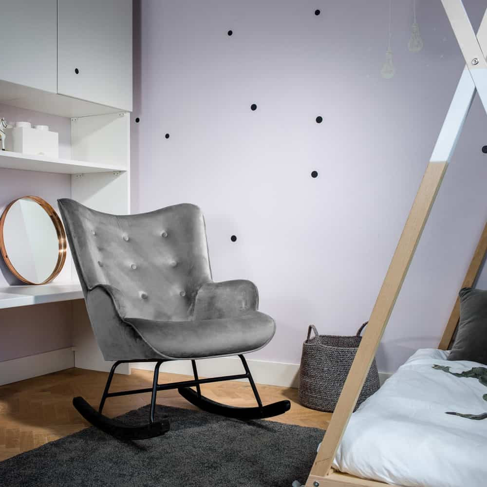 Aemely® Schommelstoel 'Steerne' in grijs velvet met zwart houten poten, geplaatst in een stijlvolle kamer naast een bed en ronde spiegel.