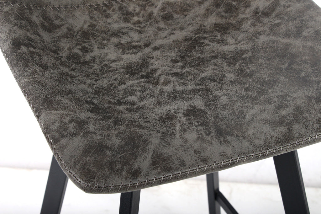 Close-up van Barkruk 'Ozan' PU Grijs met grijs PU-leer en zwart metalen onderstel, benadrukt industrieel ontwerp en ergonomische zitting voor ultiem comfort.