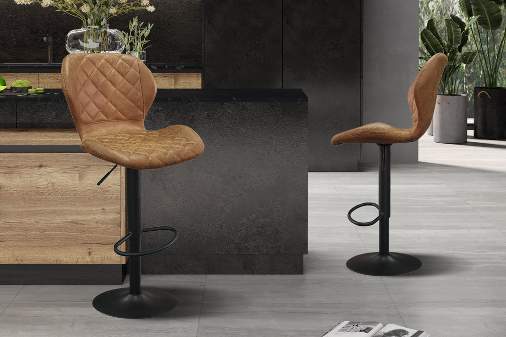 Barkruk 'Malaga' PU Cognac, set van 2, met metalen basis en vintage uitstraling, naast een plant en vaas in een stijlvolle kamer.