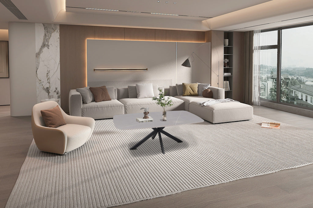 Salontafel 'Apollo' 130 cm Deens Ovaal Steen Grijs in een woonkamer, met een vaas bloemen erop, naast een witte bank en stoel.