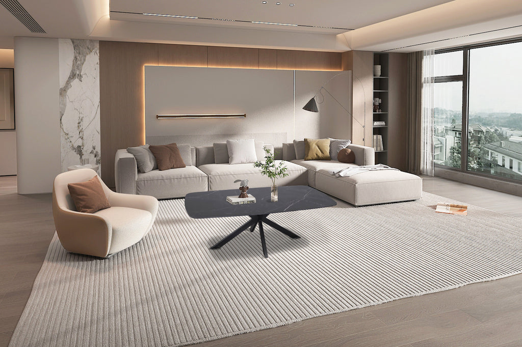 Salontafel 'Apollo' 130 cm Deens Ovaal Steen Zwart staat op een vloerkleed in een woonkamer, naast een witte stoel en een grote bank.