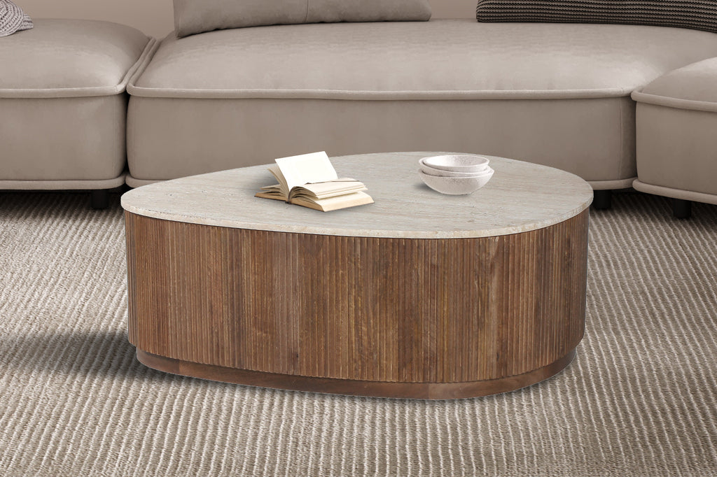 Salontafel 'Nolan' 100 cm van mango hout met travertin blad, met boek en stapel witte kommen erop, in een woonkamer setting.