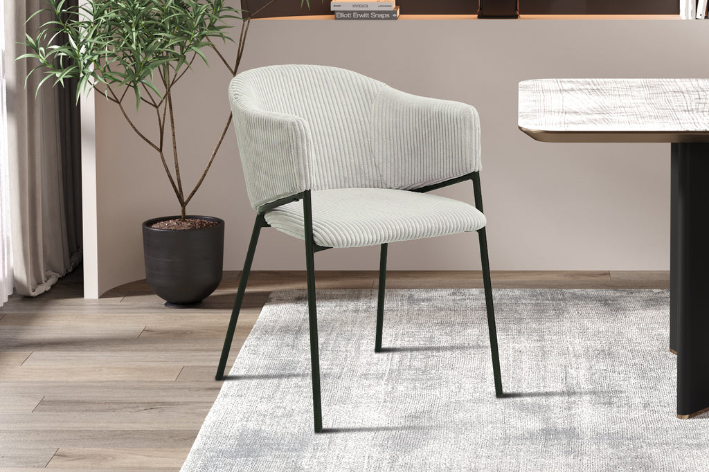 Stoel 'Hugo' Corduroy Lichtgrijs, witte stoel met zwarte poten, geplaatst in een kamer naast een zwarte pot met een kleine plant.