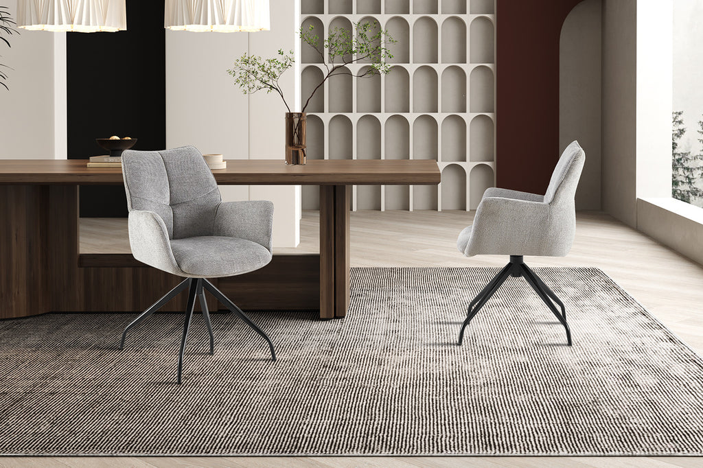 Stoel 'Lamor' draaibaar, grijs, set van twee, met metalen poten en stoffen bekleding, naast een tafel in een stijlvol ingerichte kamer.