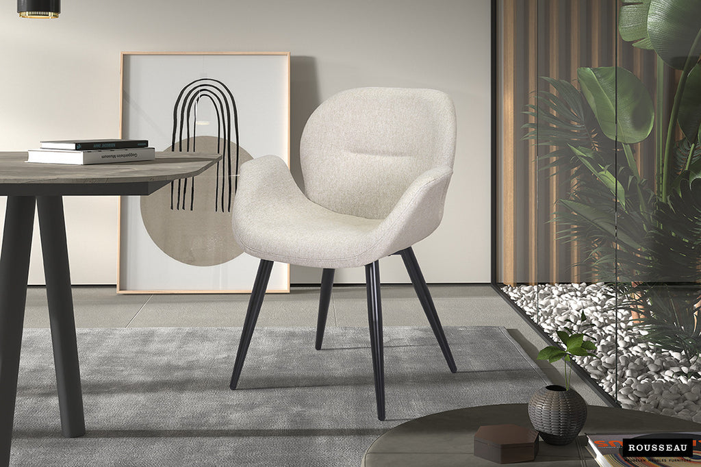 Stoel 'Maxim' Stof Beige met zwarte poten in een moderne kamer, naast een glazen wand met planten. Inclusief armleuningen, geschikt voor elke woonruimte.