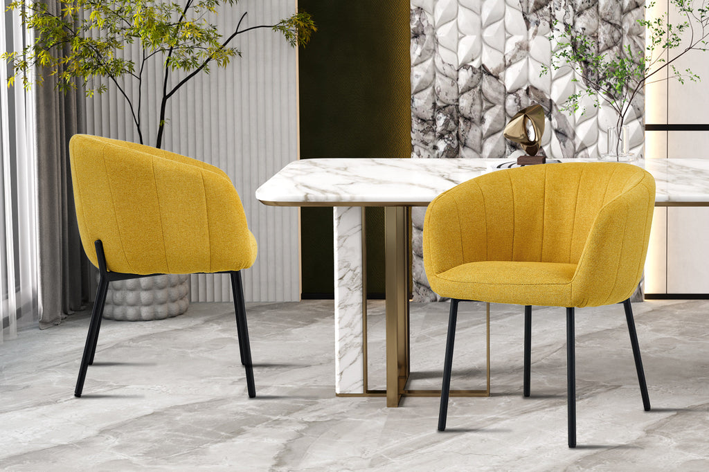 Stoel 'Sevilla' Stof Geel, met zwarte poten, naast een tafel in een moderne kamer. Verkocht per twee in een doos.