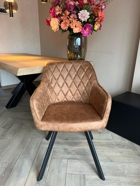 Eetkamerstoel Draaibaar 'Brione' met cognac microvezel en zwart metalen poten, naast een houten tafel met bloemen. Ergonomisch en stijlvol voor elk interieur.