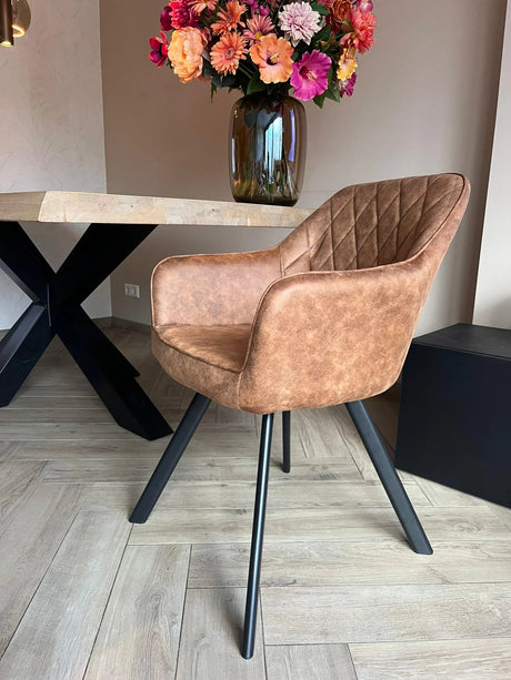 Eetkamerstoel Draaibaar 'Brione', cognackleurig met diamantpatroon en zwart metalen poten, naast een moderne eettafel met glazen vaas en bloemen.