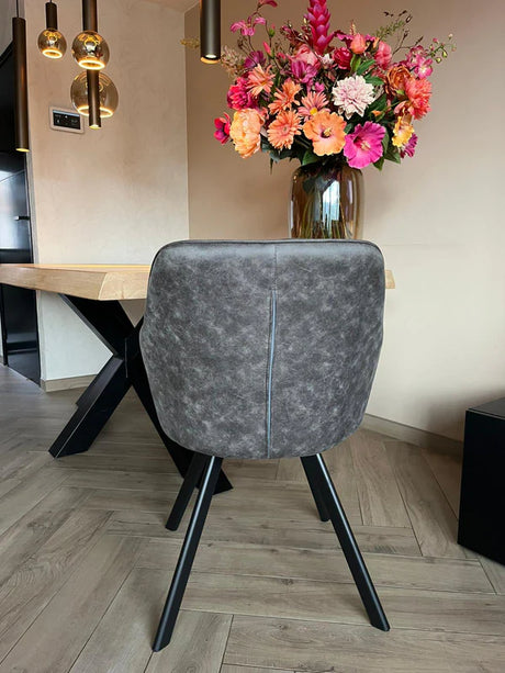 Eetkamerstoel Draaibaar 'Brione' met donkere stoffering en zwart metalen poten, naast een houten tafel met bloemenvaas en moderne hanglampen.