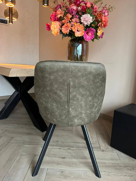 Eetkamerstoel Draaibaar 'Brione' met olijfgroene bekleding en zwart metalen poten voor een stijlvolle, ergonomische zitervaring bij een licht houten tafel in een moderne setting.