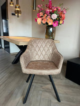 Eetkamerstoel Draaibaar 'Brione' met beige microvezel stof en zwart metalen poten, naast een houten tafel en bloemenvaas, verlicht door hanglampen.