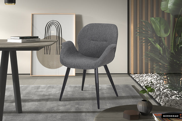 Stoel 'Maxim' Stof Grijs met zwarte poten, geplaatst in een moderne kamer met glazen wand en planten, perfect voor elk interieur.