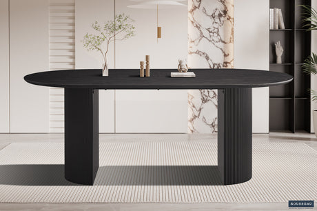Tafel 'Lagos' 200 cm ovaal decor donkerbruin, met een plant erop en een boek naast een beeldje, op een zwarte tafel.